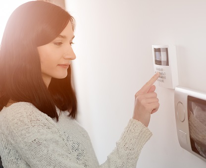 Young brunette woman entering code on keypad of home security alarm. Video intercom next to alarm keypad.