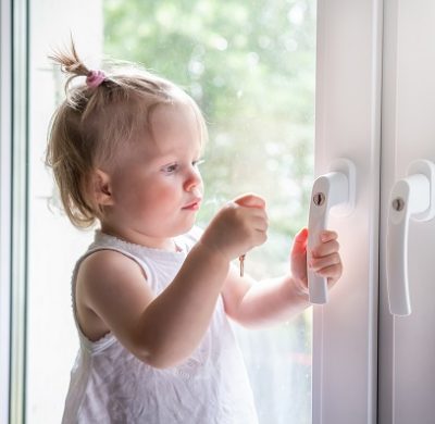 Child playing on window sill. Little baby tries open window handles on lock
