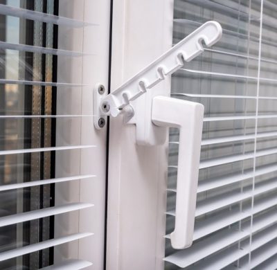 A handle and a restrictor, window stopper or limiter on PVC double glazed window with horisontal aluminium blinds close up.